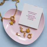 Personalised Week Of Charms Necklace in gold with interchangeable initial, birthstone, moon, star, heart, lightning bolt and horseshoe charms displayed beside meaning card.