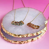 Image shows gold and rose gold 50th Birthday Birthstone Rings Necklace lying in a white coater with gold trim