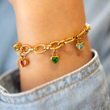 Gold charm bracelet with heart shaped charms on a person's wrist worn with a denim shirt.