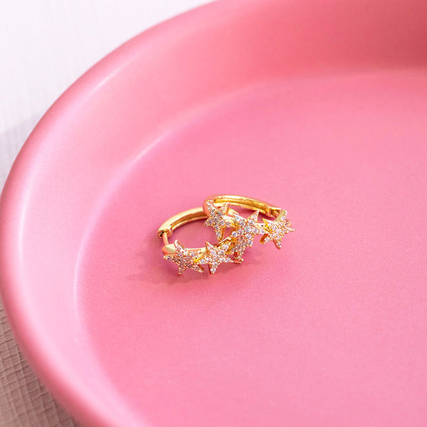 Gold plated crystal triple star huggie hoop earrings  presented on a bright pink jewellery dish