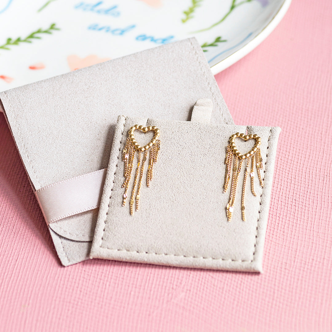 Image shows a pair of gold plated dotted heart earrings with chain drop detail on a jewellery pouch