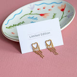 Image shows a pair of gold plated dotted heart earrings with chain drop detail on a limited edition card