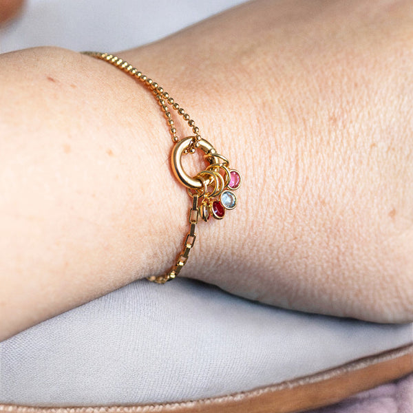 Image shows a gold family birthstone charm bracelet on a woman's wrist