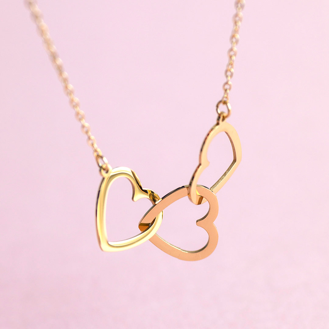 Image shows a gold plated triple interlinked heart necklace on a pink background