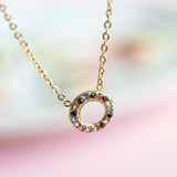 Image shows a gold multi coloured gemstone necklace on a pastel background