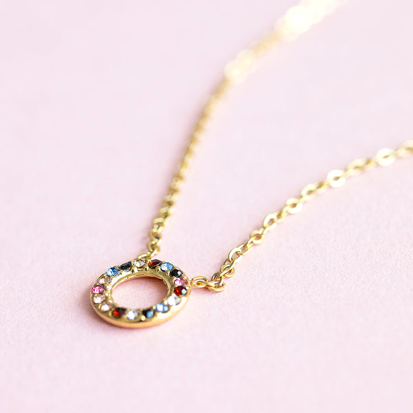 Image shows a gold multi coloured gemstone necklace on a pink background