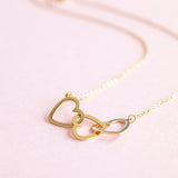 Image shows a gold plated trio heart necklace on a pink background