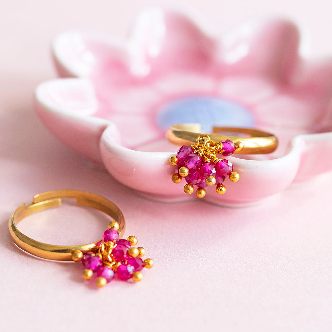 Image shows two ruby gemstone cocktail charm rings in a pink trinket dish