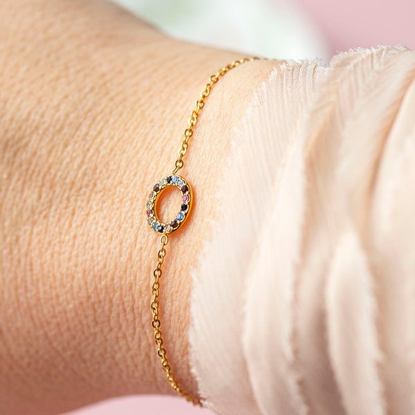 Image shows a womans wrist wearing a multi coloured gemstone set circle bracelet