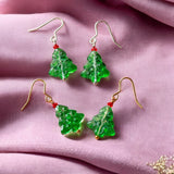 image shows two pairs of cute glass Christmas tree earrings on a dusky pink fabric background