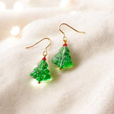 image shows a pair of glass christmas tree earrings on a cream fabric background