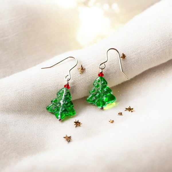 image shows a pair of glass christmas tree earrings on a cream fabric background