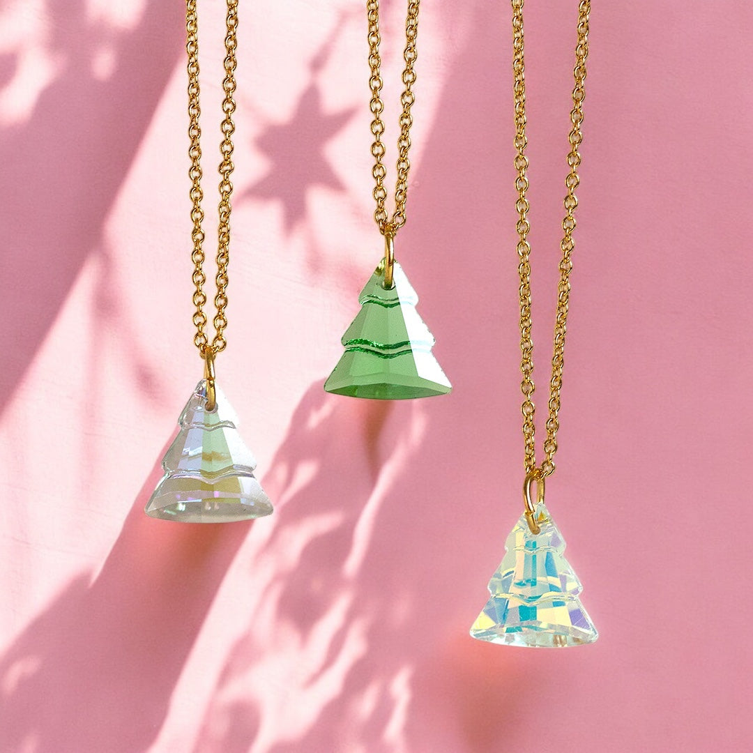 image shows three glass christmas tree necklaces hanging in front of a pink background