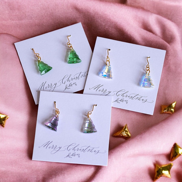 image shows three pairs of christmas tree earrings on merry christmas cards on a pink background