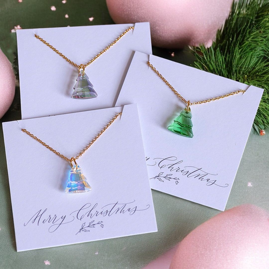 image shows three glass christmas tree necklaces on white merry christmas cards on a pink and green festive background