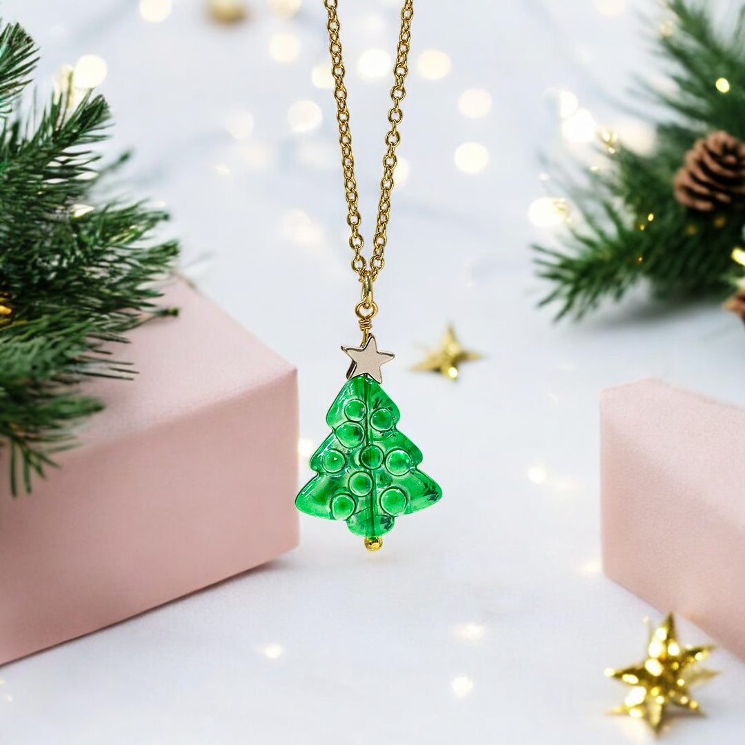 image shows a green glass Christmas tree necklace with gold star detail on a pink and spruce festive background