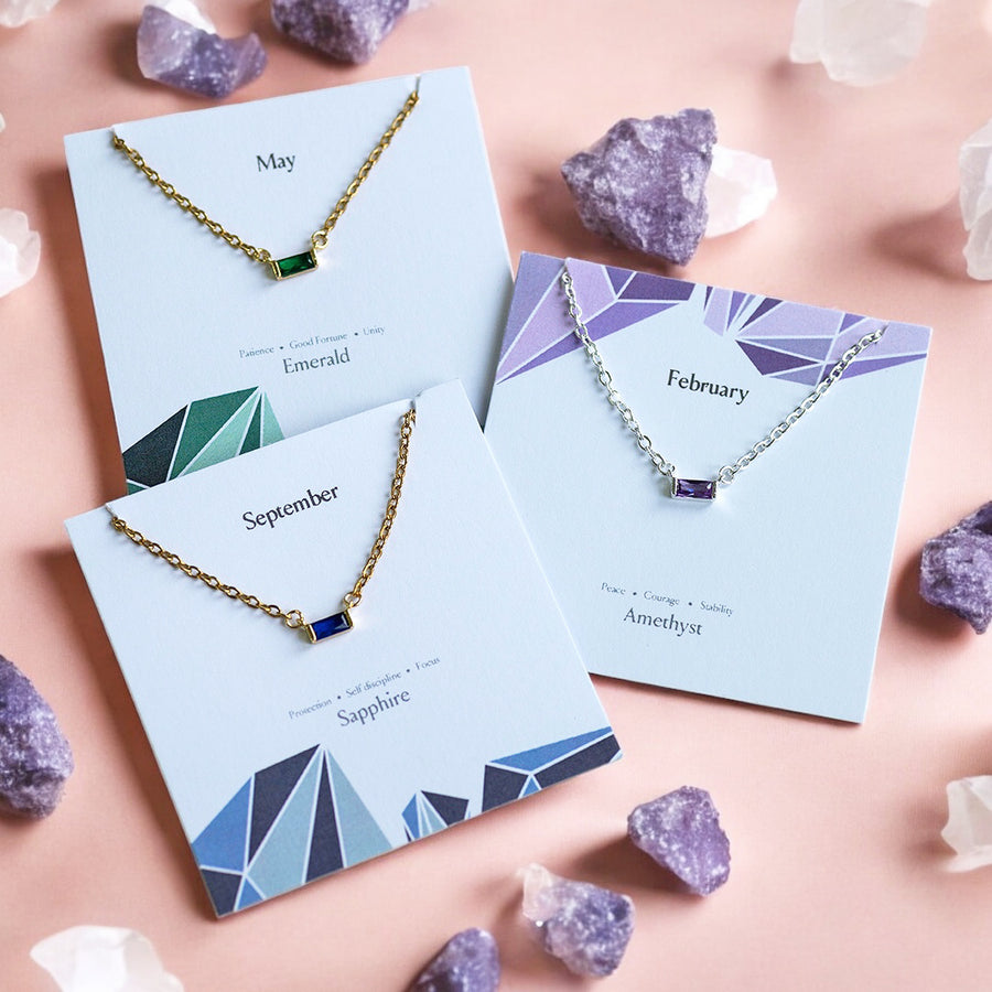 image shows a selection of birthstone necklaces displayed on birthstone characteristics cards on a peach background