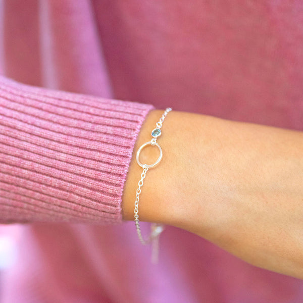 Delicate silver plated Mother and Child Circle Bracelet featuring circular charm and blue-grey birthstone, worn with a pink jumper.