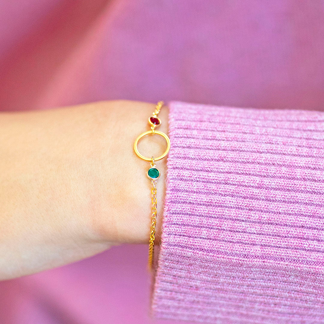 Gold plated Mother and Two Children Birthstone Bracelet with open circle charm and ruby and emerald birthstones, styled with a soft jumper for an elegant look.