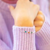 Silver plated Mother and Three Children Birthstone Bracelet featuring circular charm and three stones in teal, amber and green, styled with a lilac jumper.