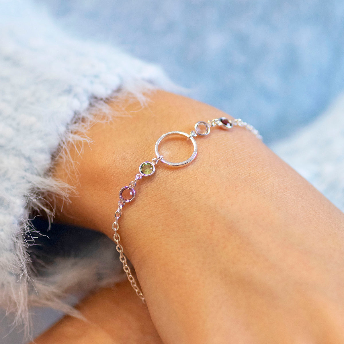 Silver plated Mother and Four Children Circle Birthstone Bracelet with four colourful stones, styled with a soft blue jumper.