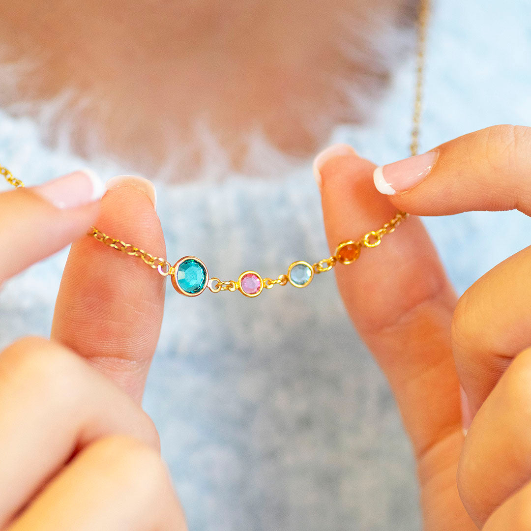 Gold plated Mother and Three Children Birthstone Link Necklace with four colourful birthstones on a delicate chain, shown worn over a soft blue knitted jumper.