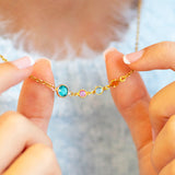 Gold plated Mother and Three Children Birthstone Link Necklace with four colourful birthstones on a delicate chain, shown worn over a soft blue knitted jumper.