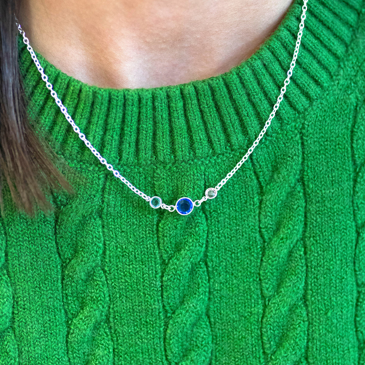 Sterling silver Mother and Two Children Birthstone Link Necklace worn on a green knitted jumper, featuring three linked birthstones in blue, green, and clear tones.
