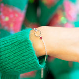 Delicate silver plated Mother and Two Children Bracelet featuring a sapphire and a ruby birthstone and circular charm, worn with a bright green jumper.