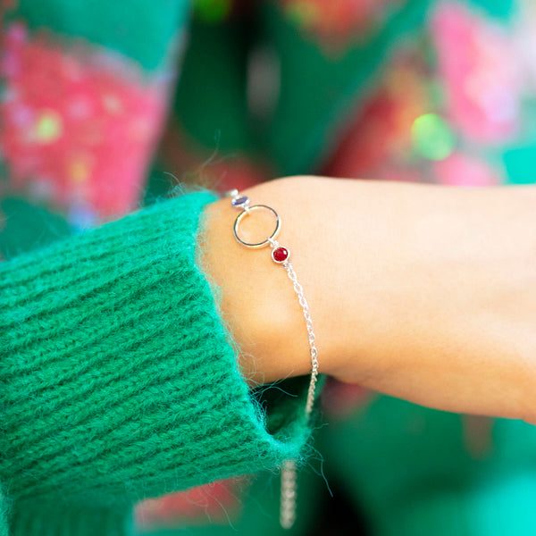 Delicate silver plated Mother and Two Children Bracelet featuring a sapphire and a ruby birthstone and circular charm, worn with a bright green jumper.