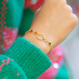 Gold plated Mother and Four Children Circle Birthstone Bracelet featuring a circular charm and four vibrant birthstones, worn with a green jumper.