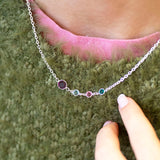 Sterling silver Mother and Three Children Birthstone Link Necklace with four linked birthstones in green, pink, clear, and deep red tones, worn with a green and pink textured jumper.