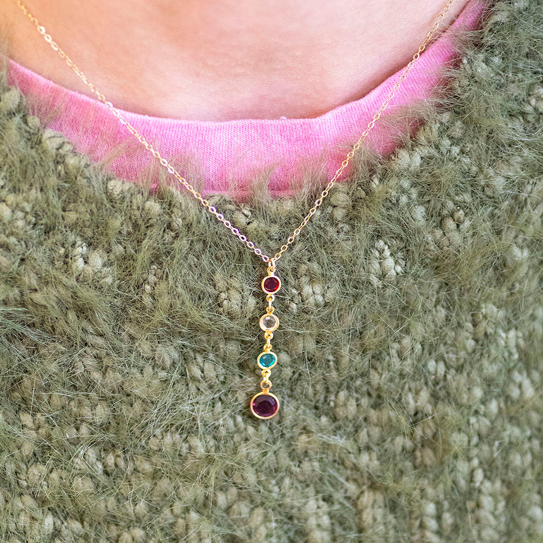 Gold necklace with colourful birthstones worn by a person against a textured green background