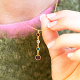 Gold plated Mother and Three Children Birthstone Pendant Necklace worn with a green jumper, showing four linked birthstones symbolising a mother and her three children.