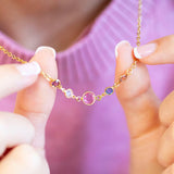 Gold necklace with colourful birthstones held by a person against a blurred background