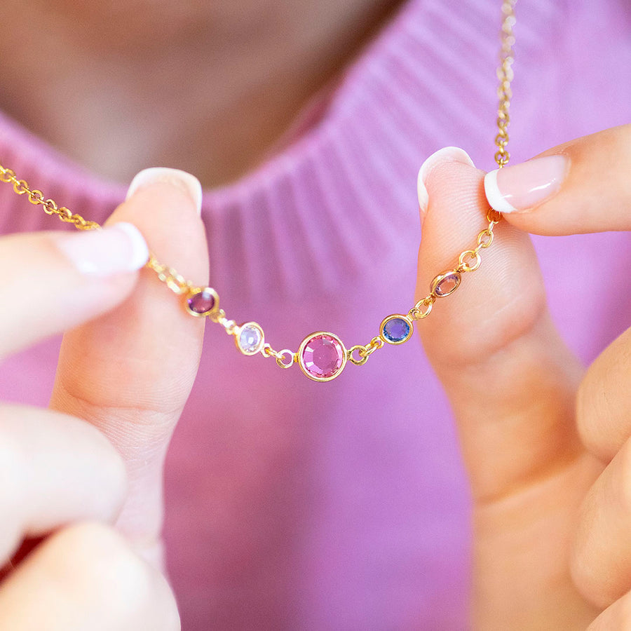 Gold necklace with colourful birthstones held by a person against a blurred background