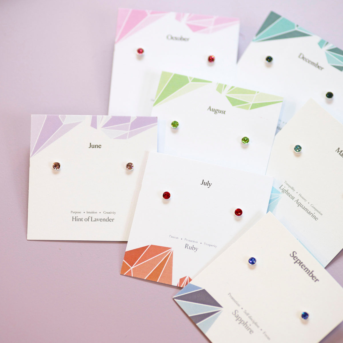 Set of minimalist sterling silver birthstone earrings arranged by month on decorative cards.