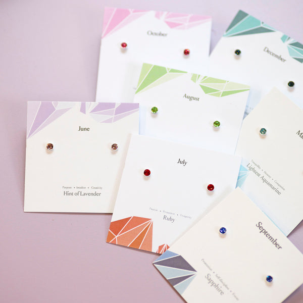Set of minimalist sterling silver birthstone earrings arranged by month on decorative cards.