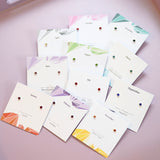 A collection of birthstone stud earrings for each month, presented on pastel birthstone cards.