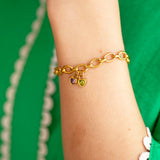 Gold charm chain bracelet with heart shaped birthstones on a wrist against a green background