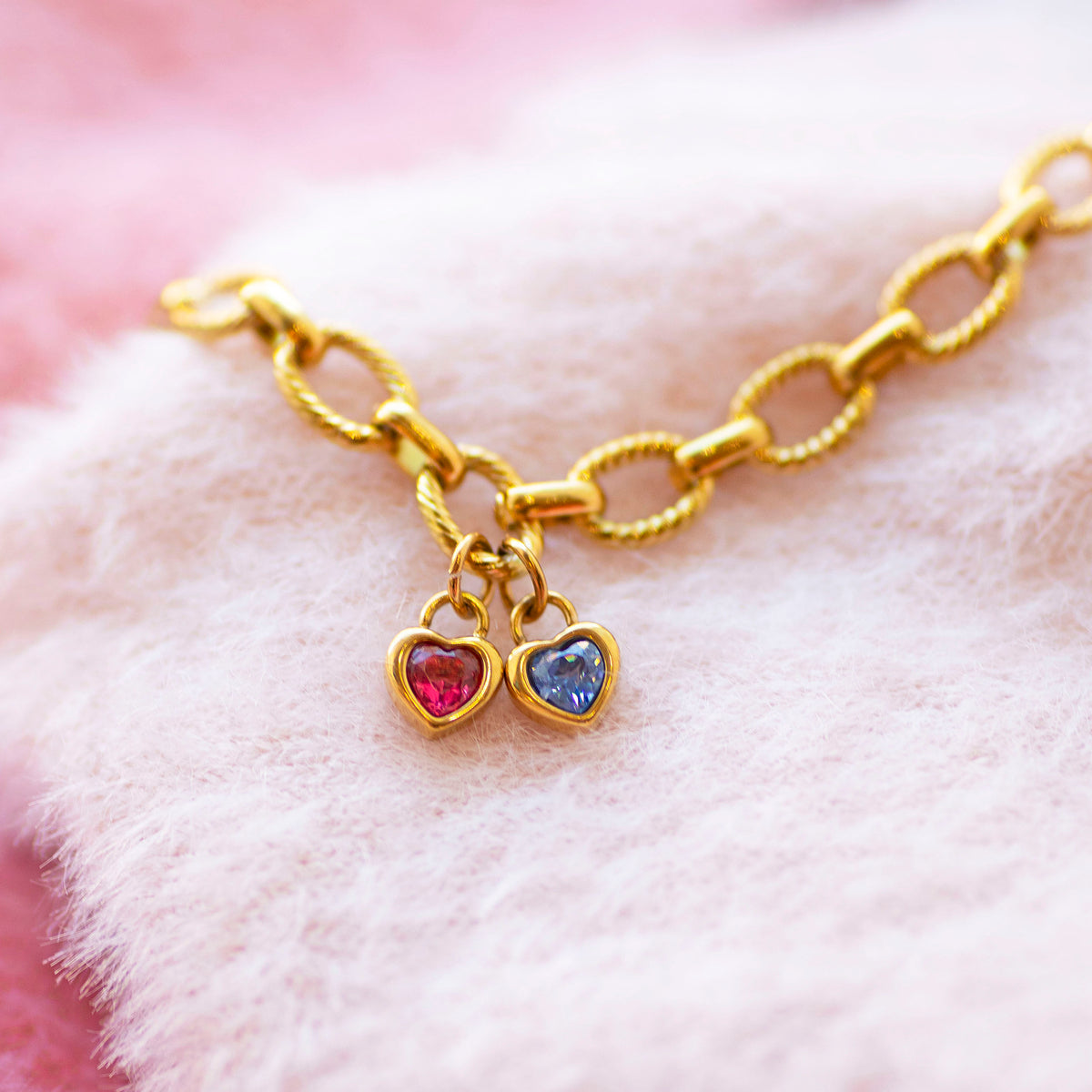 Gold charm bracelet with heart shaped birthstones on a soft pink background