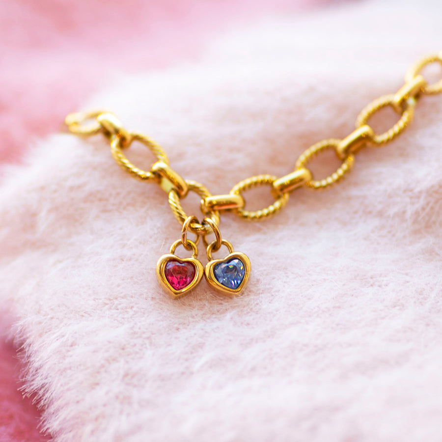 Gold charm bracelet with heart shaped birthstones on a soft pink background