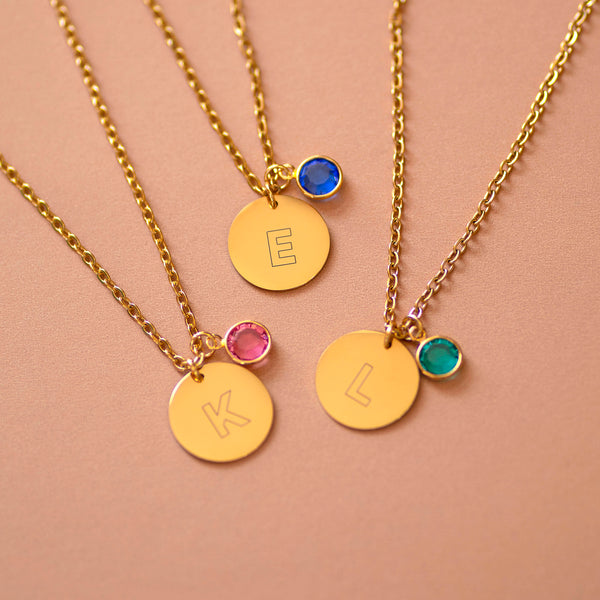 Personalised gold initial disc necklaces with birthstone charms in pink, blue and green, styled layered for everyday wear.