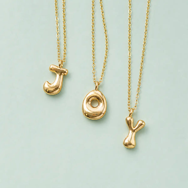 Personalised gold bubble initial necklaces with J O and Y letter pendants on a pale green background