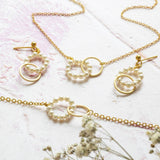 Beaded pearls eternity jewellery set lying on  pinky stone background with dried white flowers