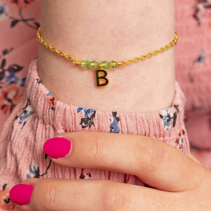 Image shows model wearing gold birthstone bracelet with B initial charm and August birthstone