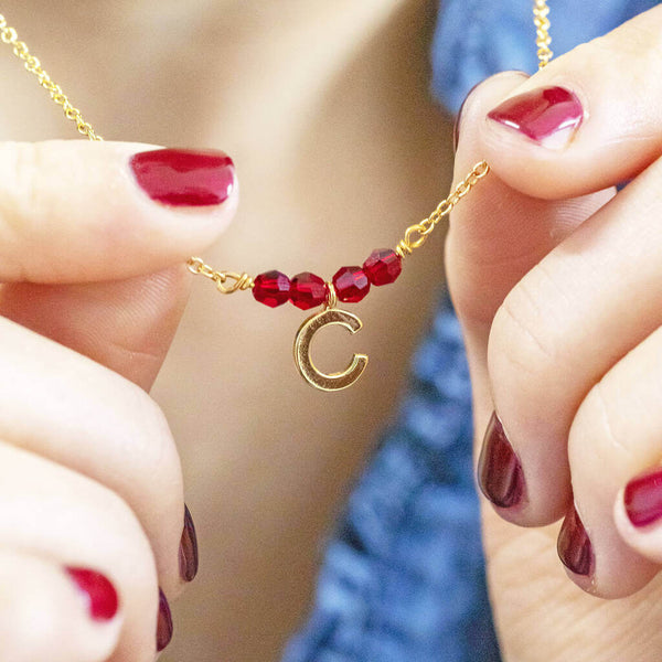 Image shows model holding birthstone bar necklace with initial charm C and July birthstone