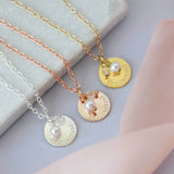 Silver,rose gold and gold bridesmaid pearl and crystal disc charm necklaces lying on a grey jewellery board with pink material below