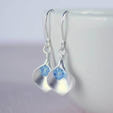 Silver calla lily birthstone earring with March birthstone crystal hanging from a white bowl