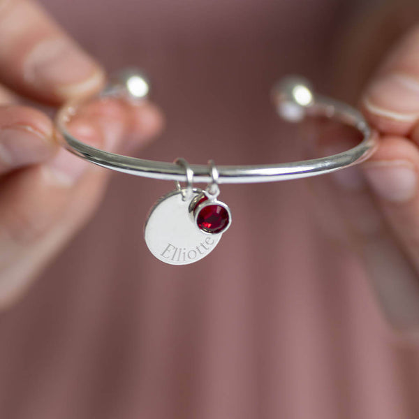 Image shows model holding Child's Personalised Disc Birthstone Bangle with the name Elliotte engraved and  July birthstone